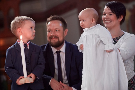 Bilete av 2 foreldre og ein stolt storebror som viser fram dåpsbarnet til forsamlinga